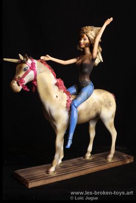 N°101: La poupée et la licorne
						Création 2026
						Dimensions: 35X30X12 cm. 
						Auteur; Loïc Jugue
						Technique : Barbie au pantalon bleu chevauchant une licorne, toutes les deux brûlées. Socle en bois de palette brûlé.
 