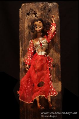 N°82: Shéhérazade rouge
						Création 2026
						Dimensions: 40X14X9 cm. 
						Auteur; Loïc Jugue
						Technique : Poupée, type Shéhérazade, avec une tunique rouge, brûlée et clouée sur une planche de palette  