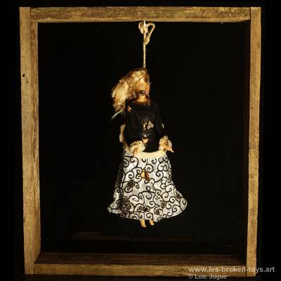 N°89: Poupée pendue
						Création 2026
						Dimensions: 50X44X10 cm. 
						Auteur; Loïc Jugue
						Technique :Poupée Barbie brûlée, haut noir, 
robe noire et blanche à motifs tarabiscotés, ficelle cadre en bois de palette. 