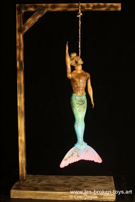 N°90: Good bye l'homme sirène
						Création 2026
						Dimensions: 62X33X19 cm. 
						Auteur; Loïc Jugue
						Technique :Poupée Ken, triton, brûlée ficelle, gibet en bois. 
