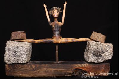 N°97: The bullet
						Création 2026
						Dimensions: 30X41X12 cm. 
						Auteur; Loïc Jugue
						Technique :Poupée Barbie brûlée,  une balle, 2 poids en métal, 2 pavés de granit, socle en bois brûlé. 