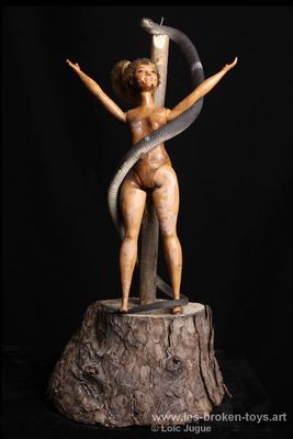 N°98: L'invention du mal
						Création 2026
						Dimensions: 44X22X20 cm. 
						Auteur; Loïc Jugue
						Technique :Poupée Barbie ronde, brûlée, serpent en plastique, bois. 