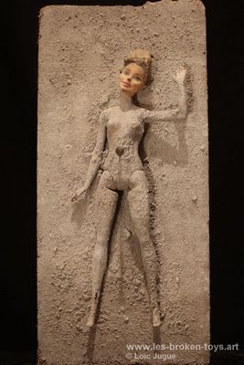 N°85: Femme de cendre, 
						Création 2020, 
						Dimensions: 40X19X11 cm. 
						Auteur; Loïc Jugue
						Technique : Poupée femme (Barbie), recouverte de cendre, clouée sur du bois recouvert de cendre.